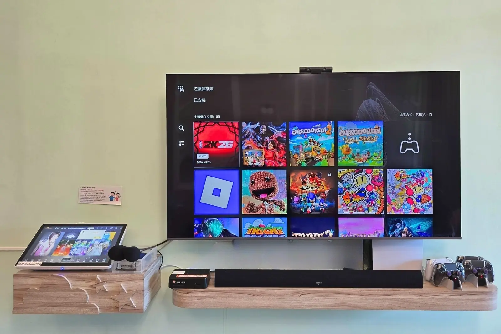 客廳電視顯示 PS5 遊戲主畫面,旁有控制器與點歌設備